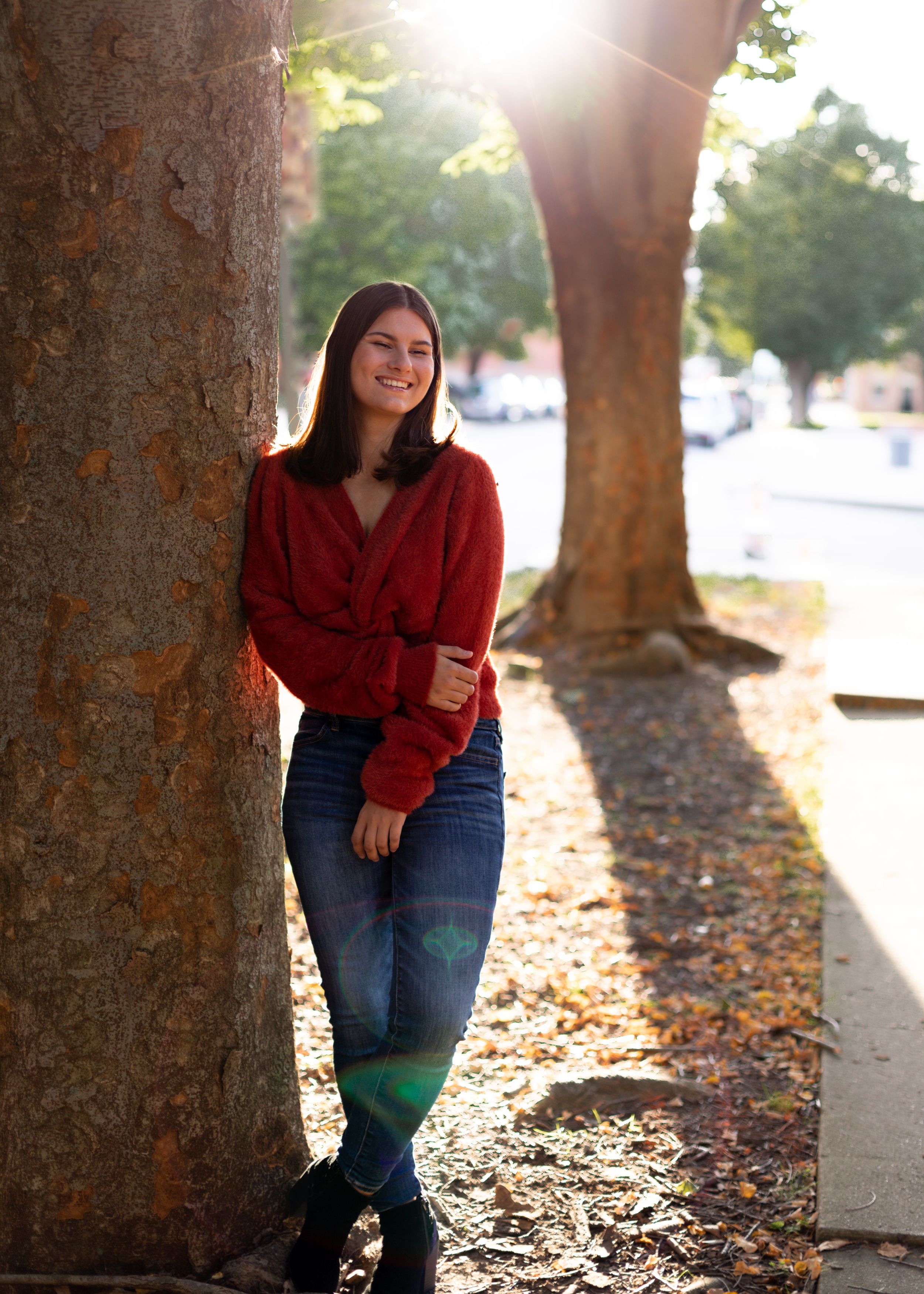 Autumn photoshoot between trees with fallen leaves and sunlight filtering through the branches.