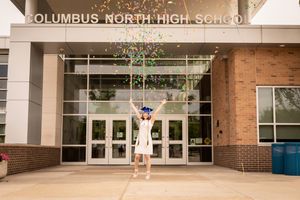 Graduate celebrating with confetti in front of Columbus North High School entrance.