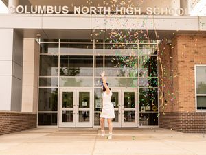 Celebratory graduation photo with confetti at Columbus North High School entrance.