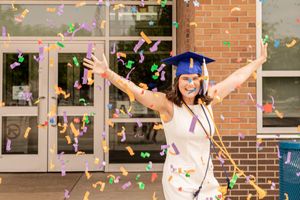 Joyful graduation celebration with colorful confetti outside school entrance.
