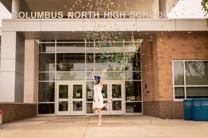 Graduate jumping with arms raised in celebration outside Columbus North High School.