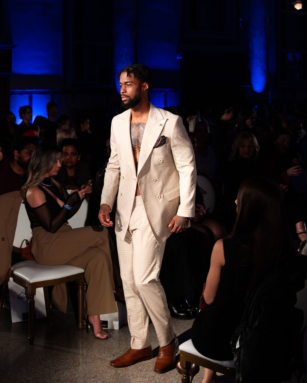 A model walks the runway in an elegant cream-colored suit with brown shoes at a fashion show.