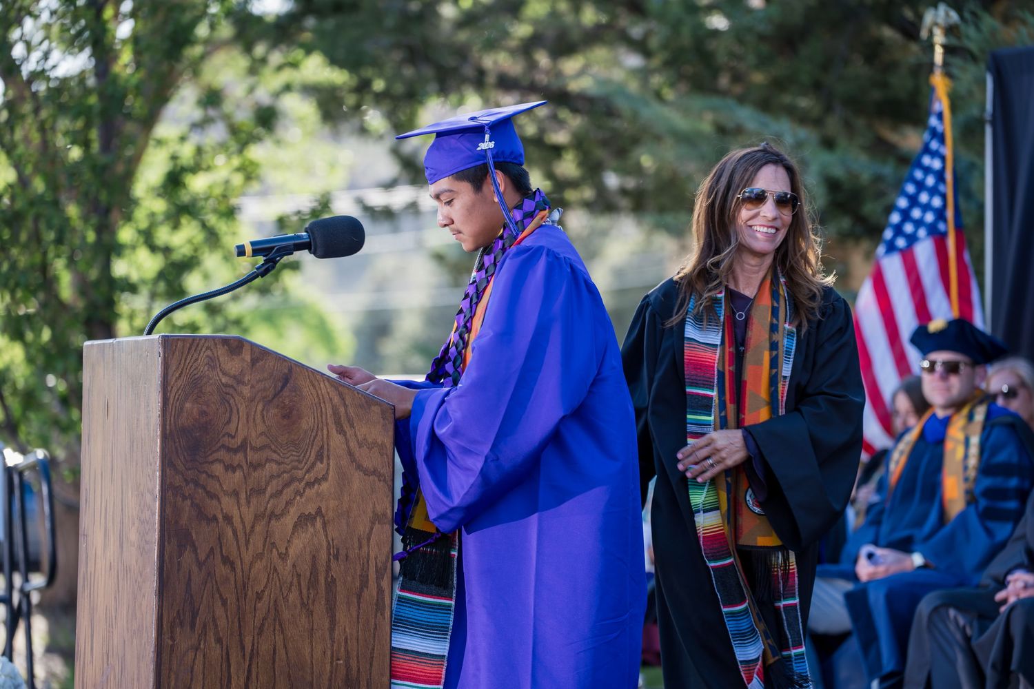 Large group of graduates in blue robes toss their caps in celebration outdoors.