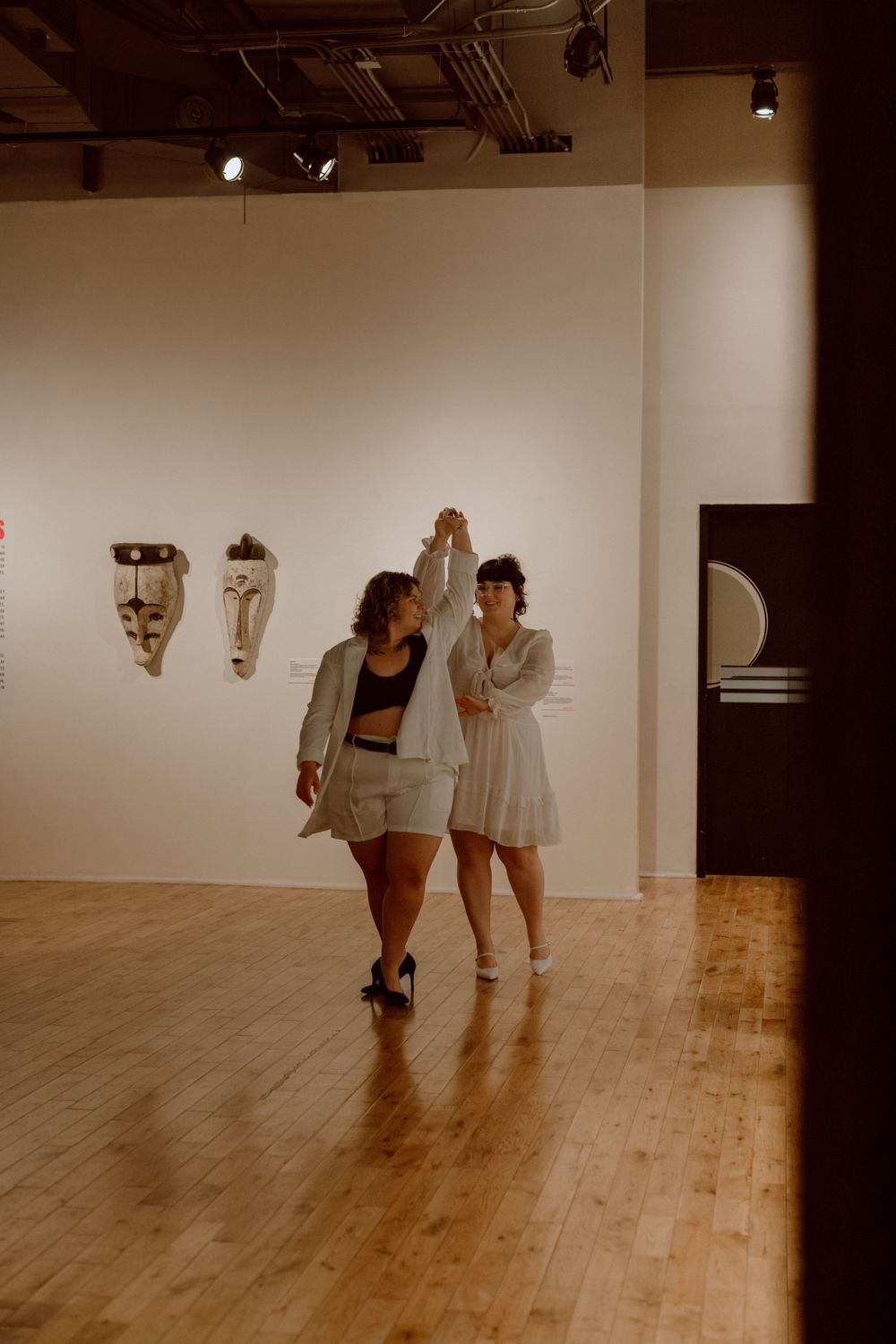 Two people dance together in a bright art gallery space with wooden floors.