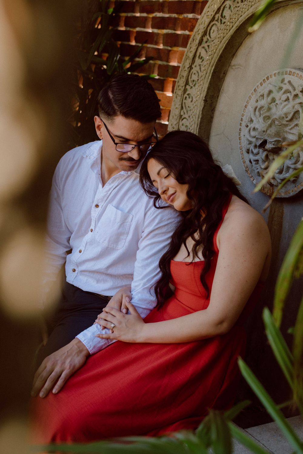 Romantic couple in white shirt and red dress sitting together in intimate engagement photo session.