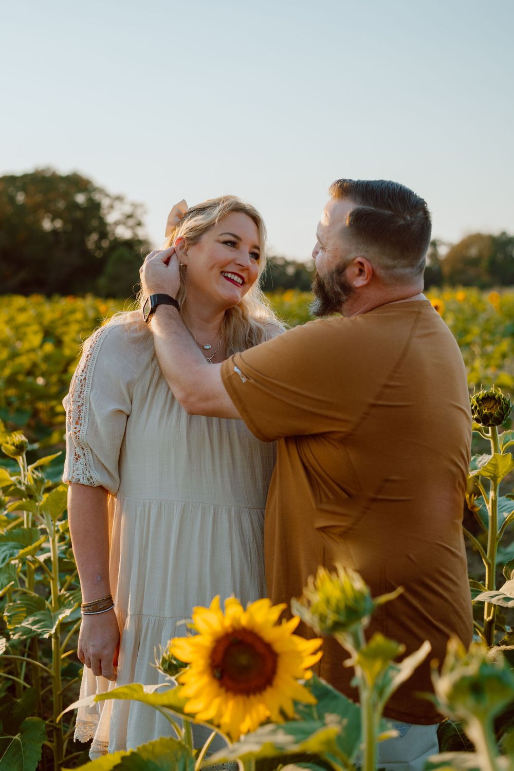 Joyful couple laughing together in a field of blooming sunflowers during sunset.