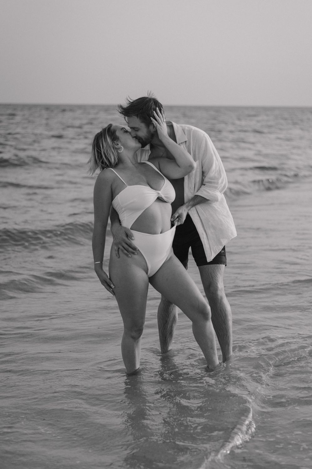 Couple sharing romantic moment in ocean waves wearing swimwear.