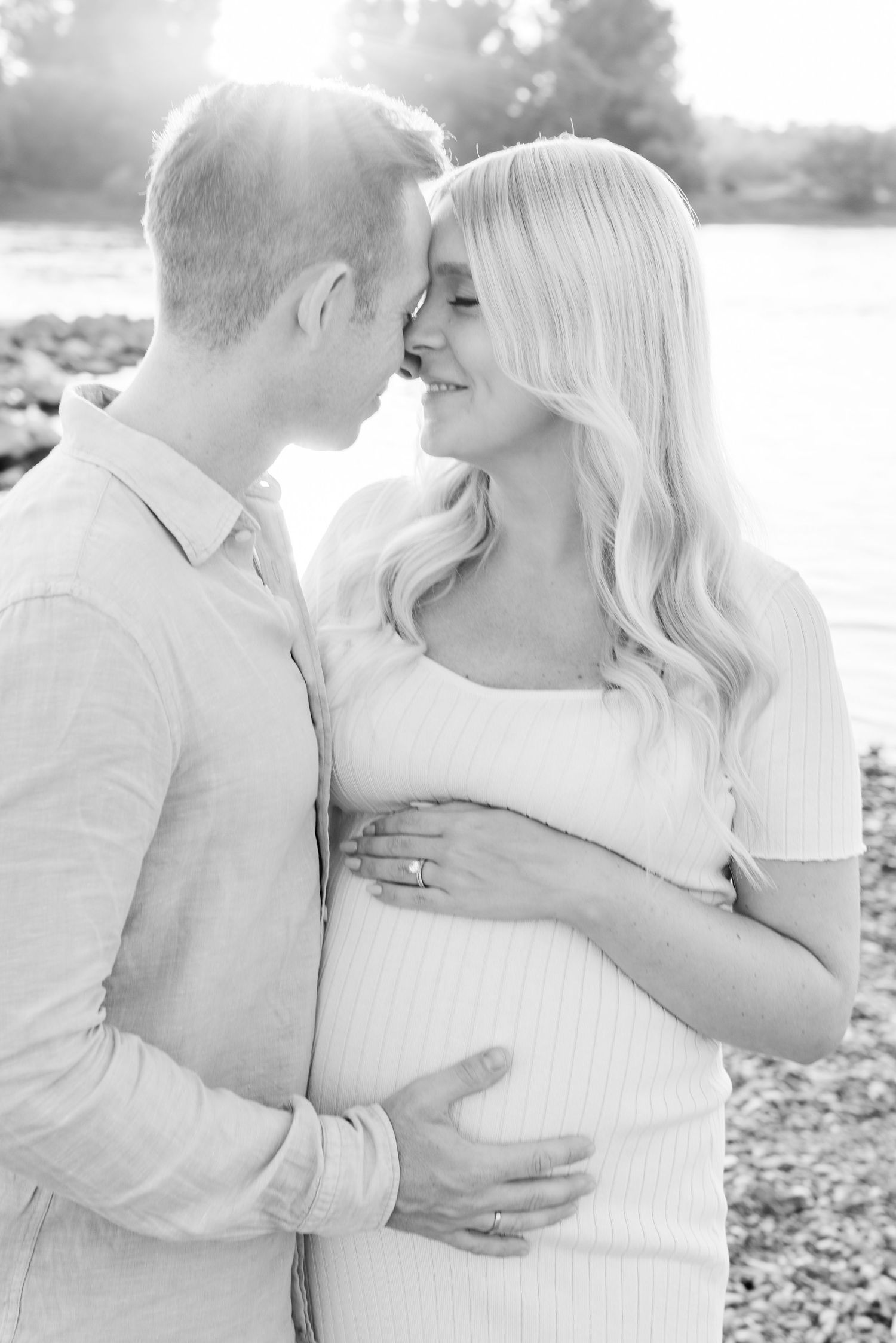 An intimate black and white maternity photo of an expectant couple by the water.