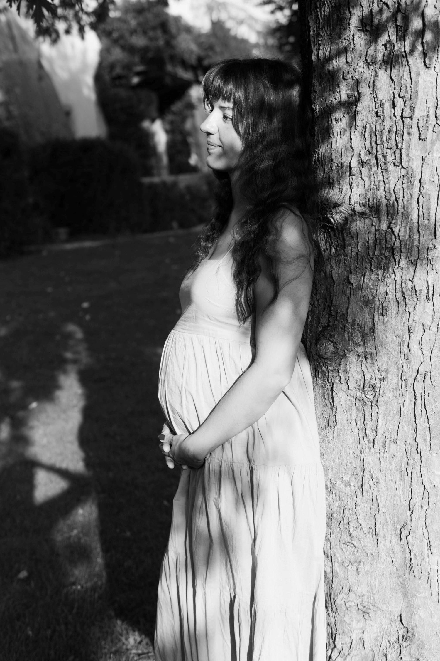 A pregnant woman is leaning against the tree.