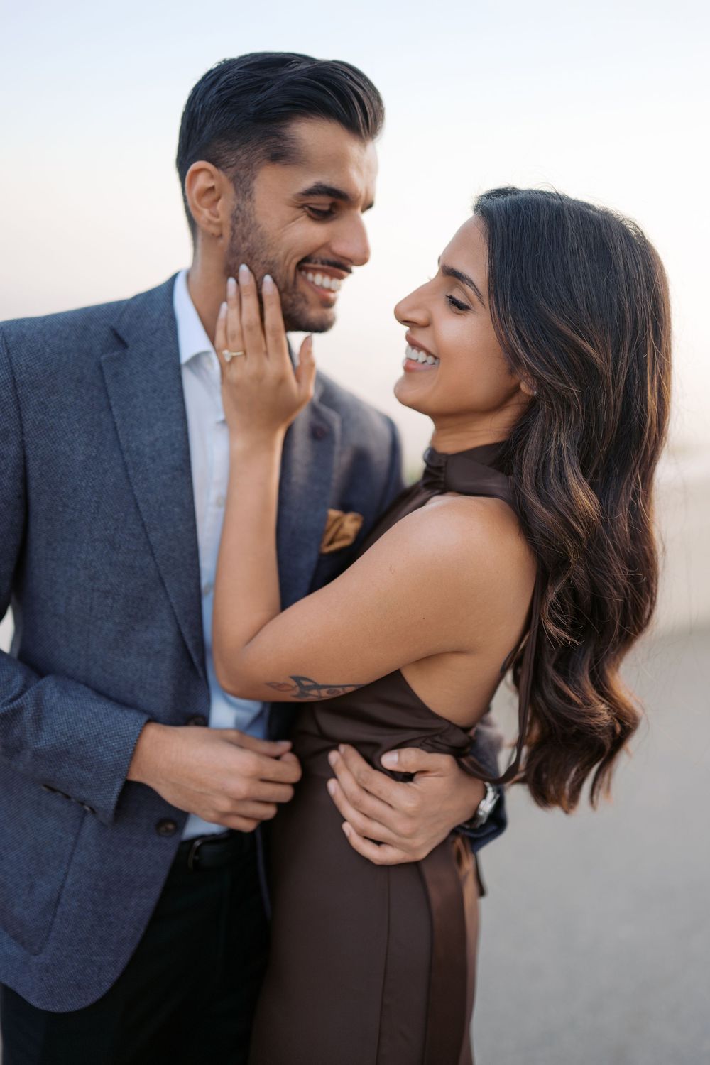 A couple shares intimate moments in a romantic desert photo session at sunset, wearing formal attire.