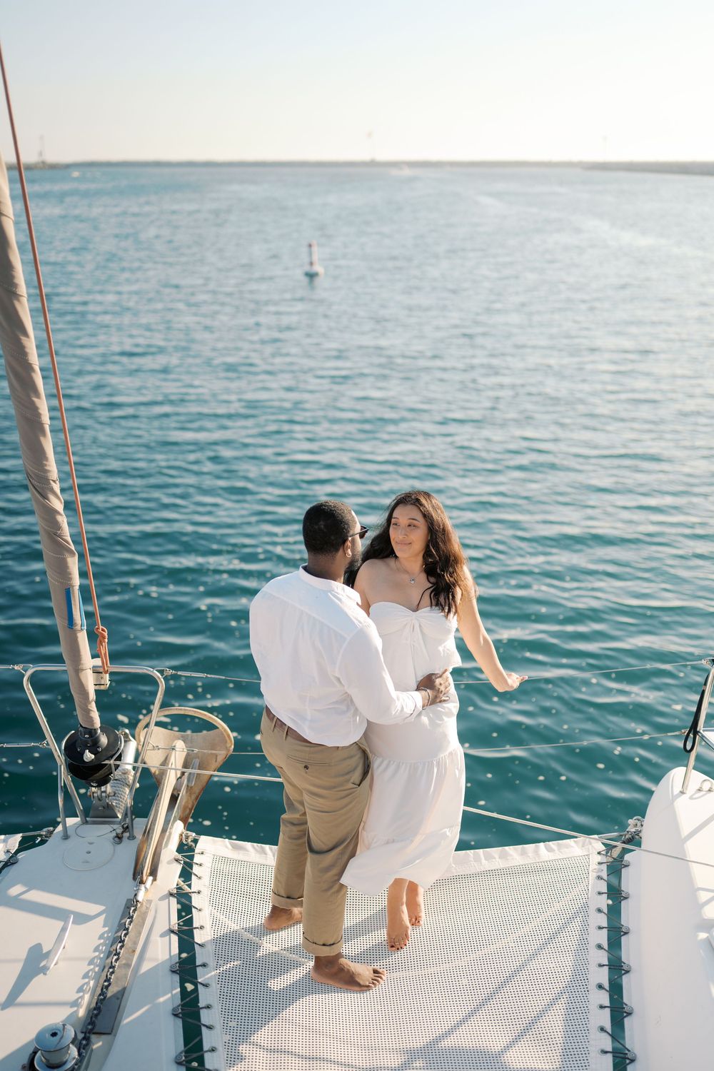 Couple in white attire dancing on a sailboat bow with turquoise ocean waters in the background.