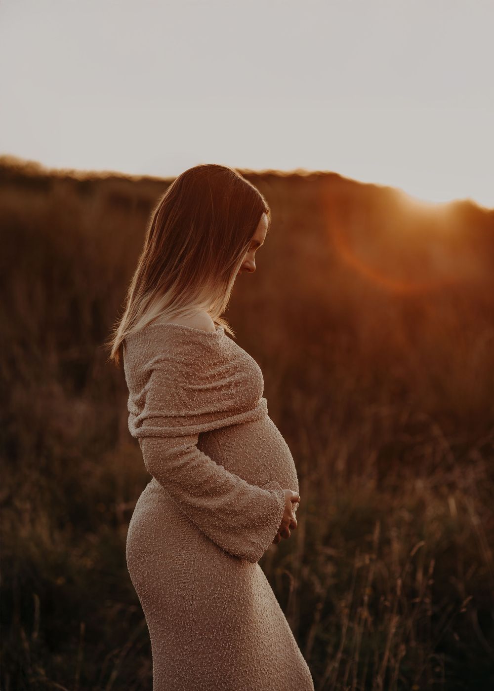 A silhouetted figure in a cozy sweater stands in a golden field at sunset, creating a warm and atmospheric scene.