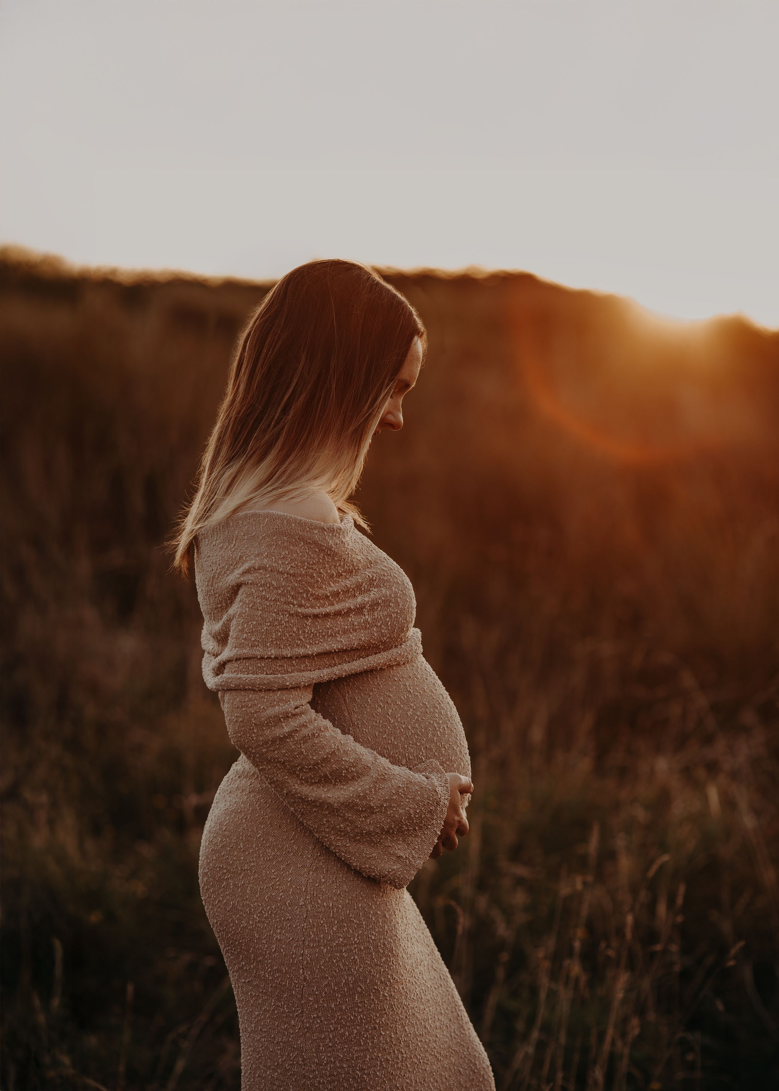 A silhouetted figure in a cozy sweater stands in a golden field at sunset, creating a warm and atmospheric scene.