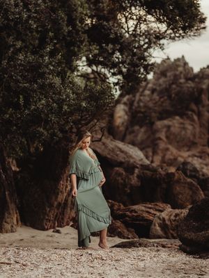 Woman in flowing teal dress poses on rocky beach terrain during golden hour photoshoot.