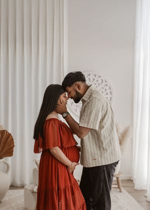 Romantic couple shares tender moments in minimalist white room, woman in flowing red dress.