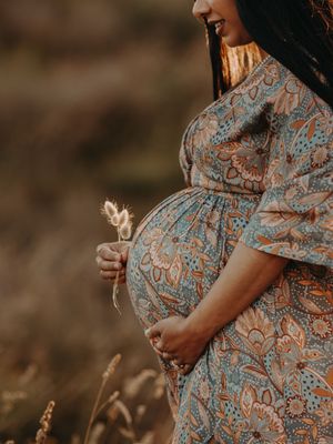 Close-up view of a pregnant belly in a floral dress against a warm sunset background with wheat stalks.