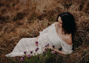 A couple in wedding attire lies in a field of tall grass and wildflowers during sunset.
