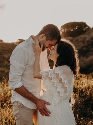 A couple in white outfits share a romantic embrace at sunset in a golden field.