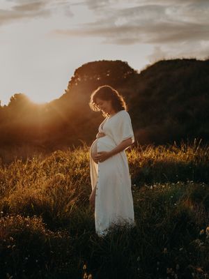 Silhouette of a person in a white dress standing in a field during golden hour sunset.