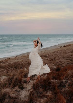 Couple in wedding attire embraces on a scenic coastal cliff at sunset with ocean waves crashing below.