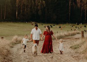 Family with dog walking together on rural path through golden field at sunset.