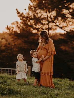 Maternity portrait with children touching belly at sunset in grassy field.