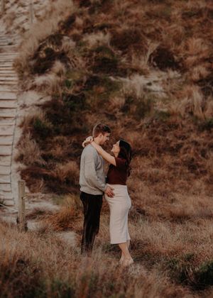 A couple embraces in a romantic moment on a hillside with warm brown tones and rustic scenery in the background.