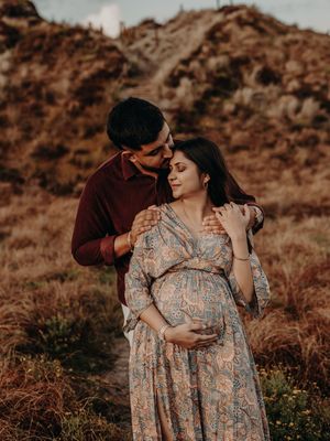 A couple embraces in a tender moment during a maternity photoshoot against a golden mountainous backdrop at sunset.