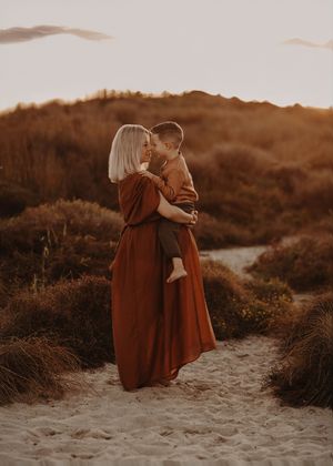 A tender moment captured at sunset on a sandy path through autumn-toned coastal foliage.