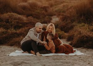 Couple resting on a white blanket in an autumn field during sunset, surrounded by golden brown foliage.