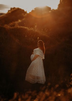 A silhouetted figure in a flowing white dress stands against a warm, glowing sunset creating a dreamy ethereal scene.