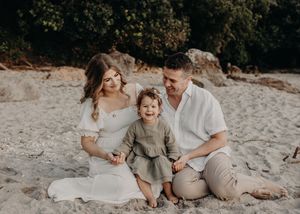 A family sits together on a sandy beach wearing neutral colored clothing during a lifestyle photo session.