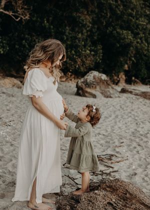 A touching maternity moment on the beach with a small child reaching up to touch a pregnant woman's belly.