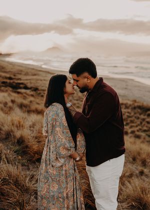 A couple shares an intimate moment at sunset in a golden desert landscape with dry brush grass and moody skies.