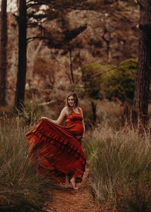 A woman in a flowing red dress twirls gracefully on a forest path surrounded by tall trees in moody lighting.