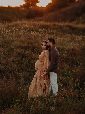 A couple embraces in a meadow at sunset, silhouetted against the warm golden light.
