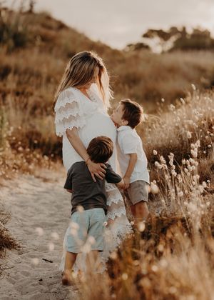 Family spending a golden hour moment together on a dirt path surrounded by dry grass and wildflowers at sunset.