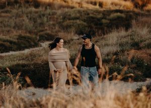 Two people walking together on a hillside trail at sunset through golden dried grass and brush.