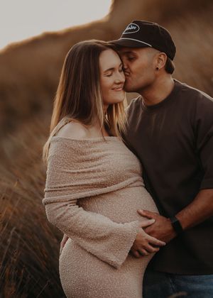 A couple embraces tenderly in a field during golden hour, with the person wearing a cozy beige sweater.