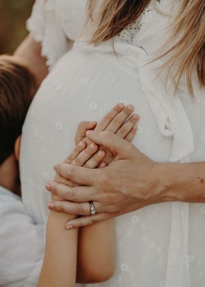 Two hands tenderly clasped together, with a sparkling engagement ring visible on one hand against a white fabric background.