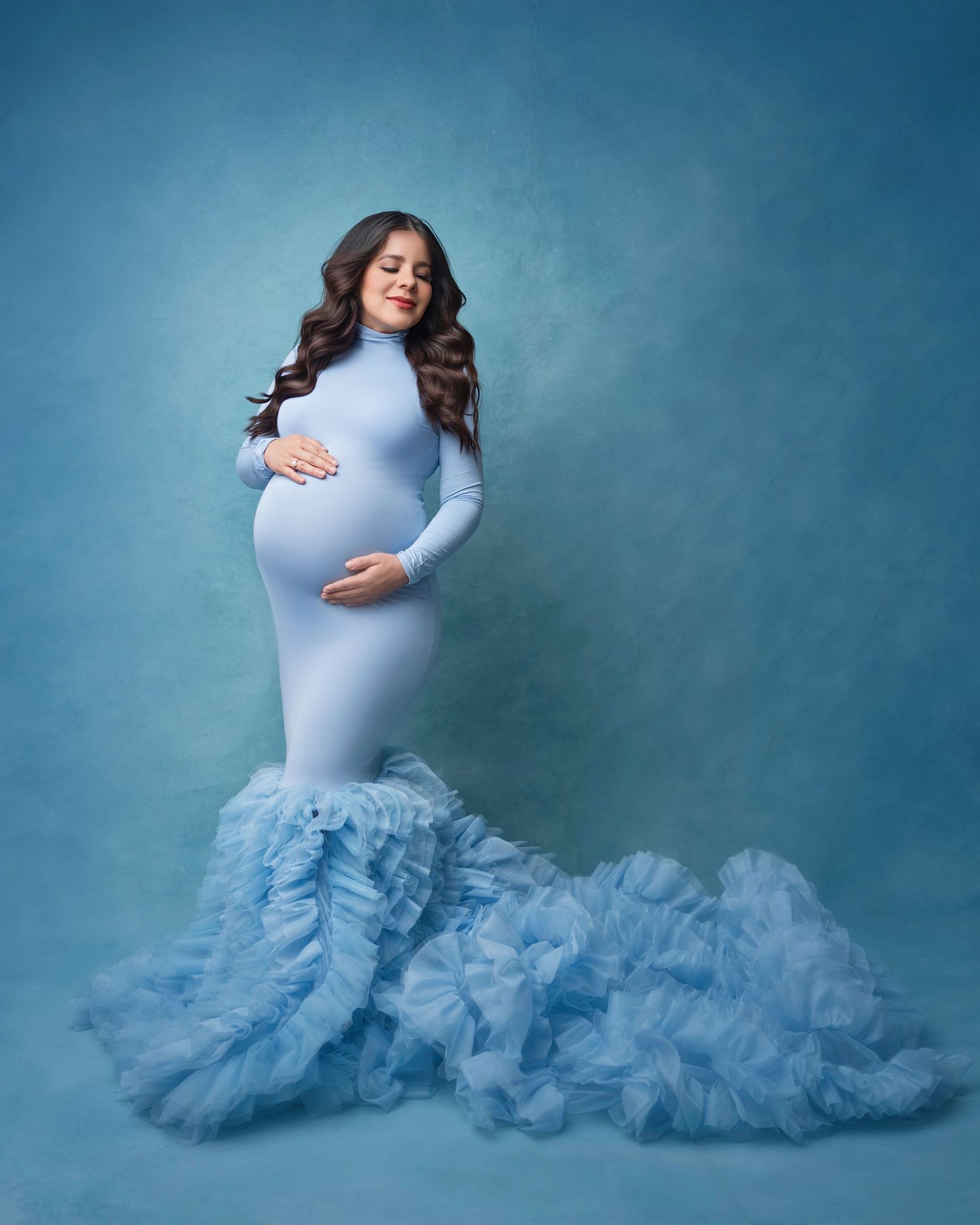 Ethereal maternity photoshoot featuring a light blue tulle gown against a dreamy blue backdrop.