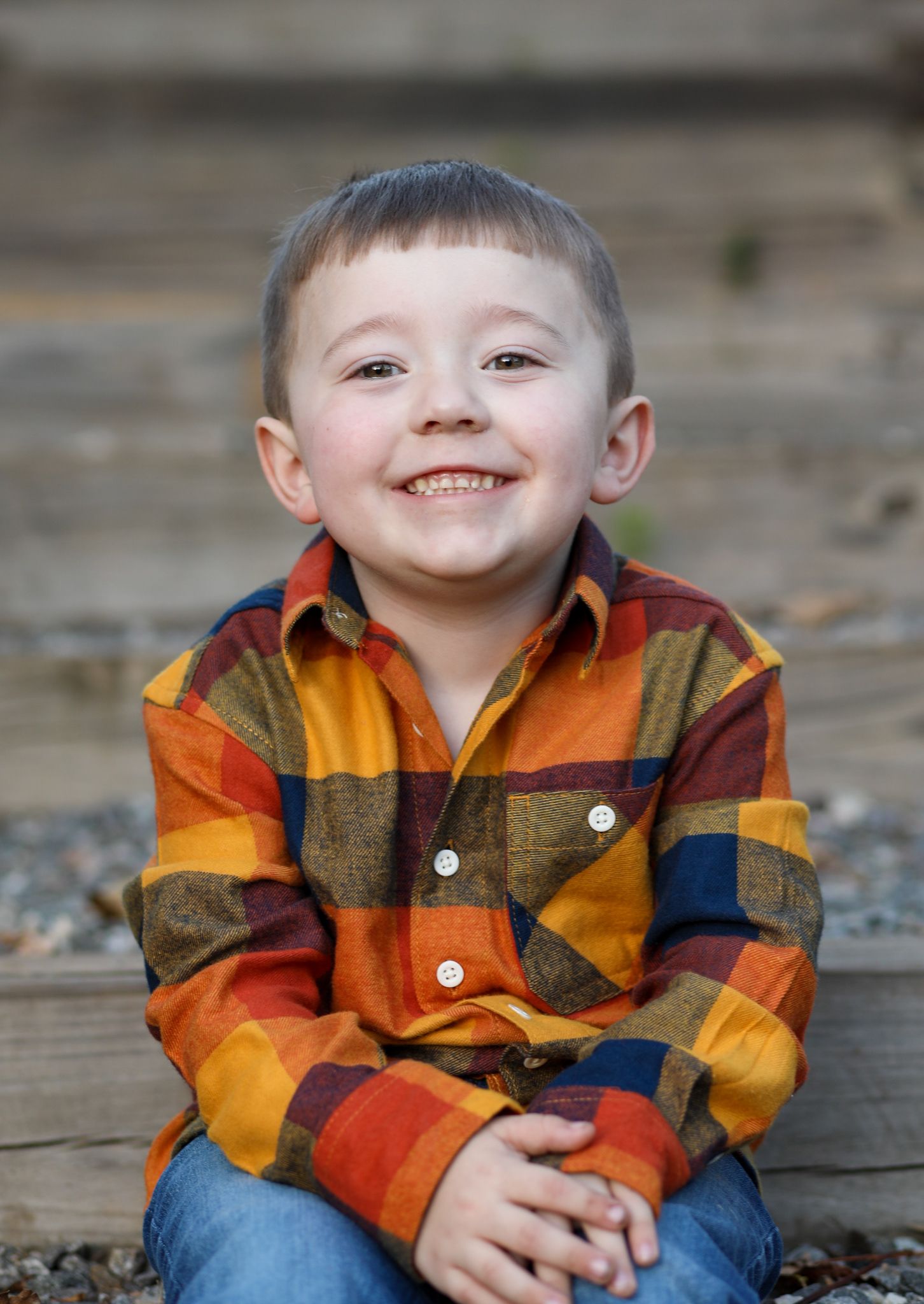 Happy young boy in colorful plaid shirt smiling while sitting outdoors in fall setting.