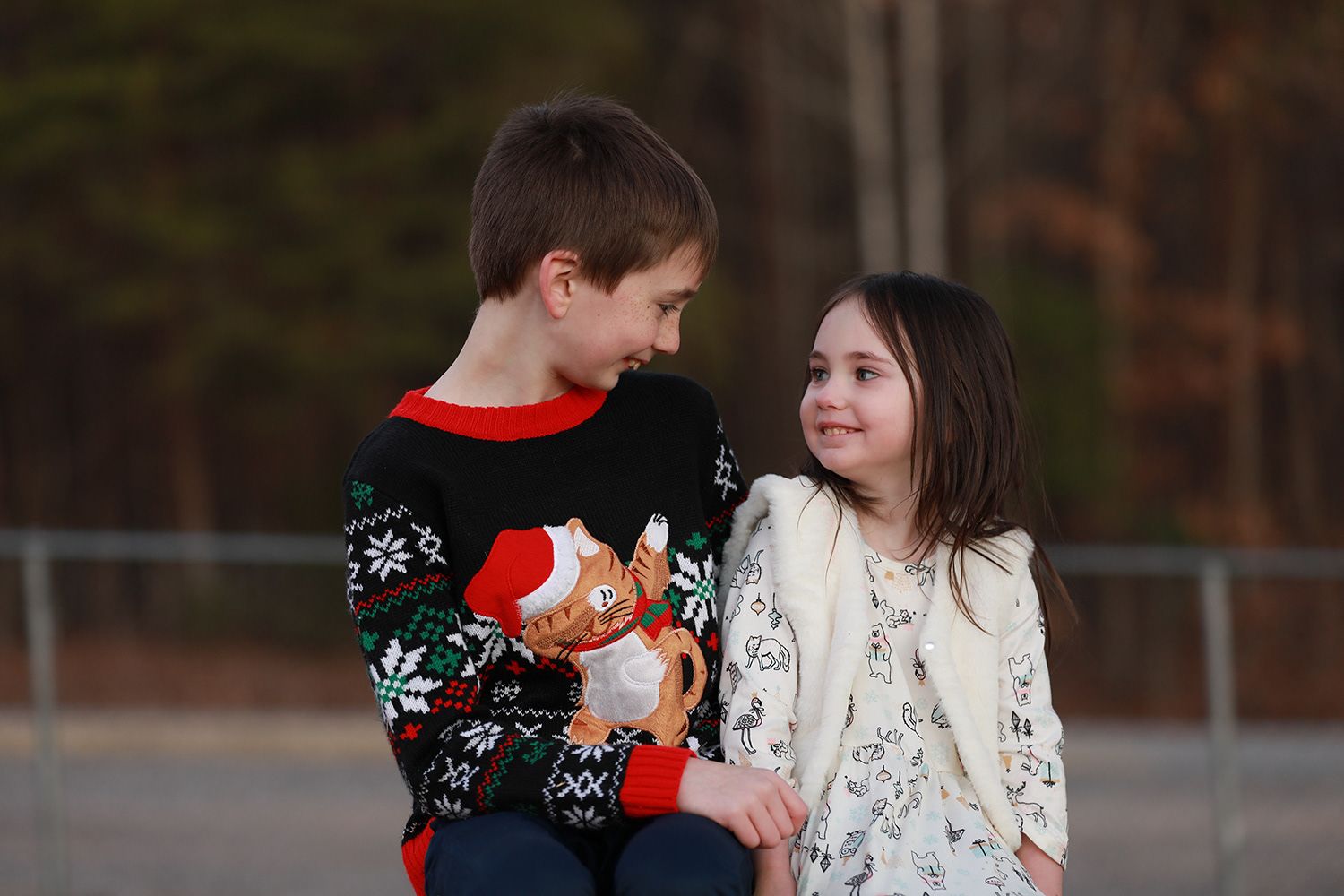 Two children in holiday sweaters share a sweet moment together outdoors at dusk.