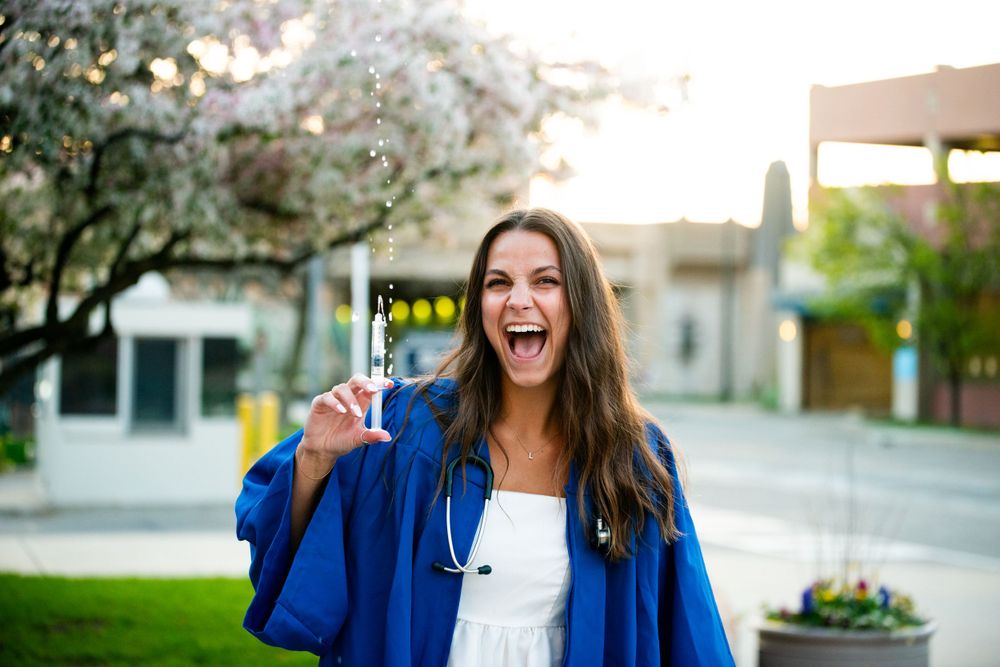 Graduate in blue cap and gown celebrating outdoors with excited expression.