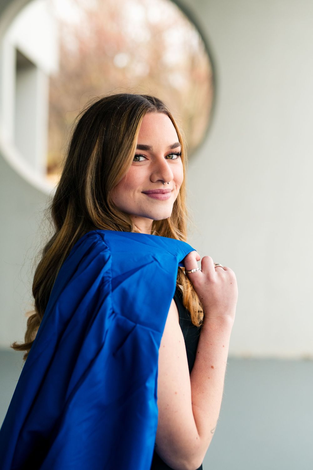 Portrait of a woman wearing a vibrant blue dress posed against a light colored wall with a round mirror in the background.