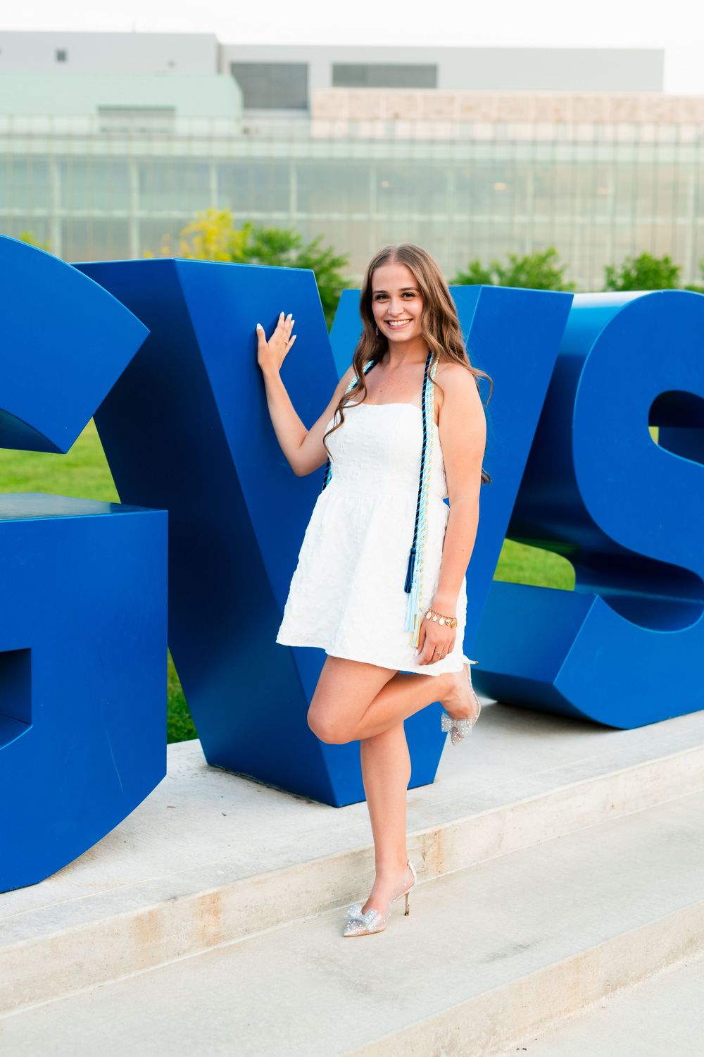 A person in a white summer dress poses against large blue sculptural letters outdoors in a photo series.