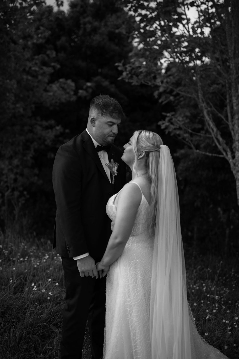 Black and white photo of a romantic wedding couple embracing outdoors in a garden setting.