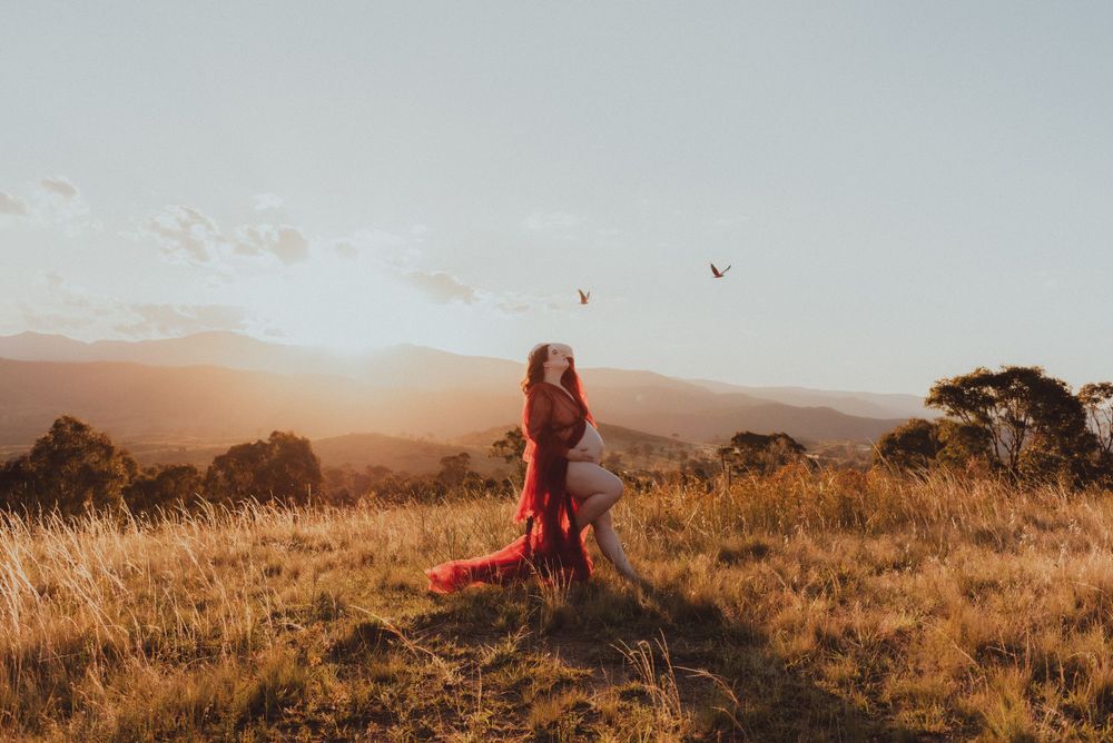 Person in red dress stands in grassy field during golden sunset.