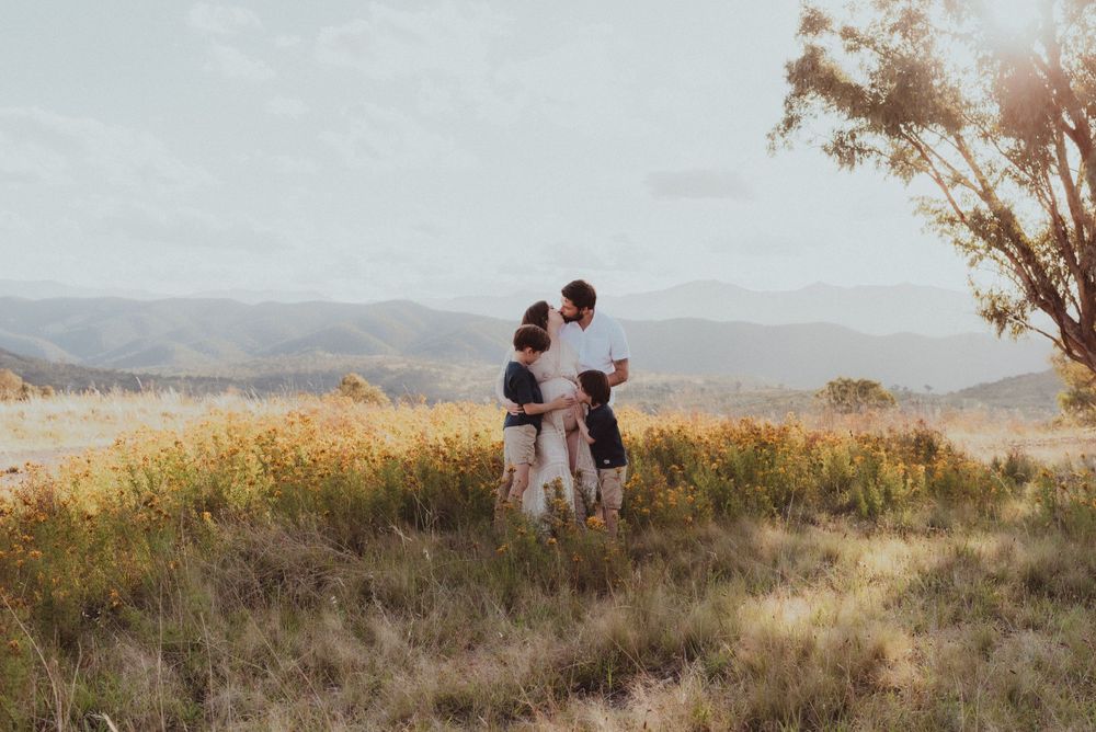 Couple embraces on hilltop during golden hour with mountains in distance.