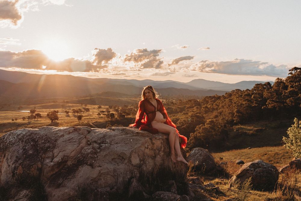 Person in red dress sits on rocky ledge during golden hour with mountain vista.